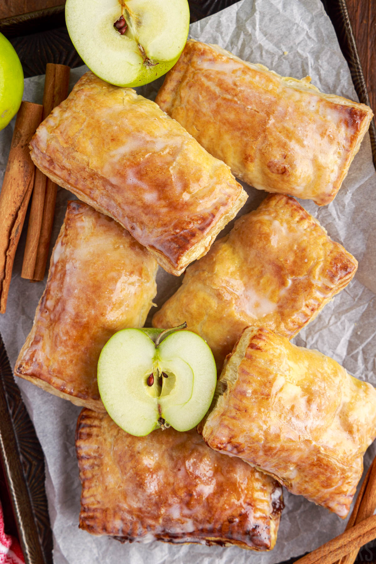 pile of apple turnovers on a tray with cinnamon sticks and fresh apple halves