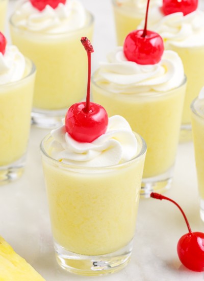 pineapple and coconut jello shots with Malibu rum decorated with whipped cream and maraschino cherries
