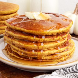 maple syrup running over a stack of pumpkin pancakes topped with butter