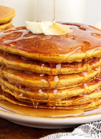 maple syrup running over a stack of pumpkin pancakes topped with butter