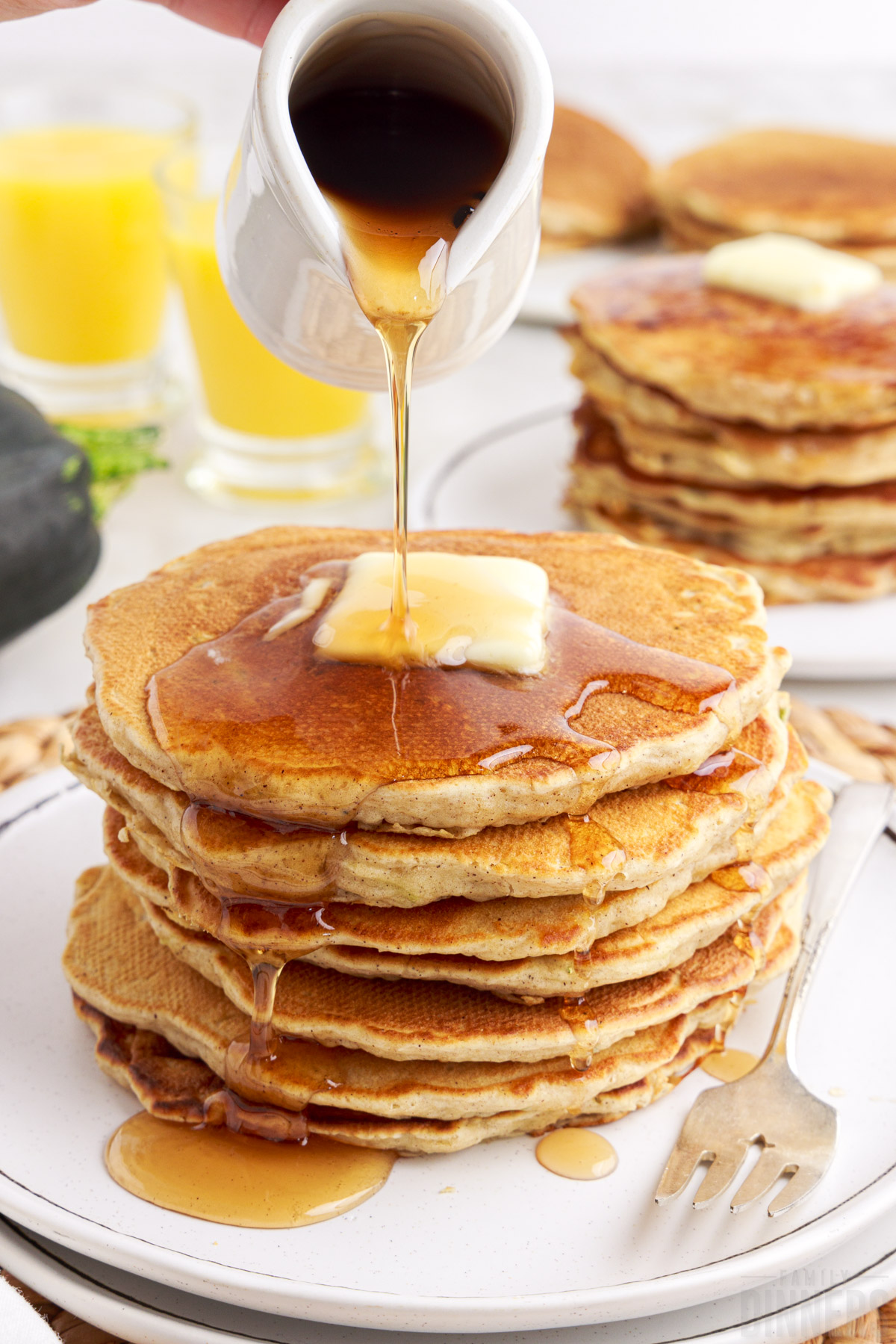 Stack of zucchini pancakes with syrup pouring on top.