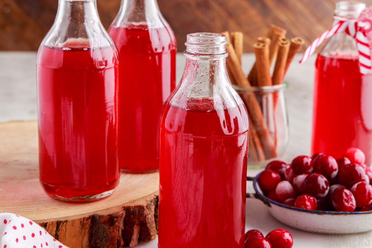 bottles of cranberry simple syrup with a bowl of fresh cranberries