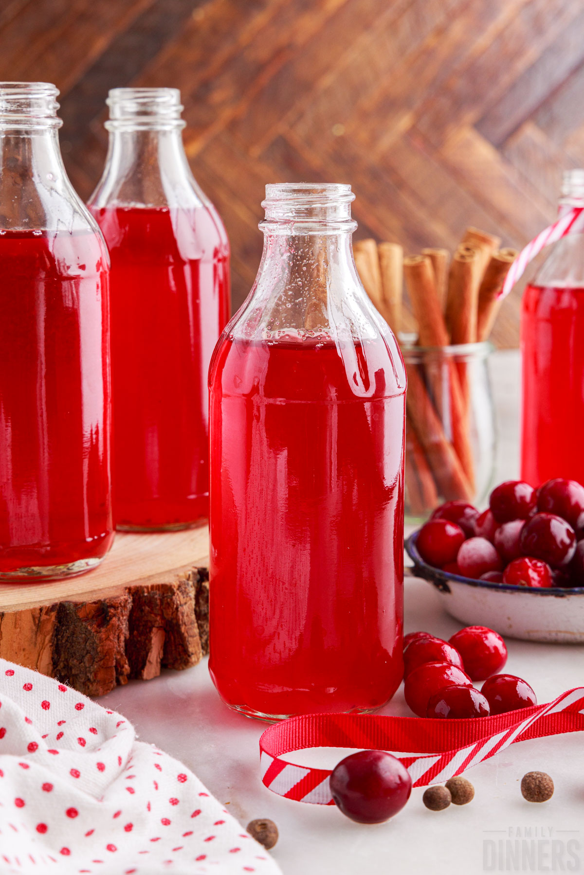 three bottles of cranberry simple syrup with fresh cranberries and cinnamon sticks