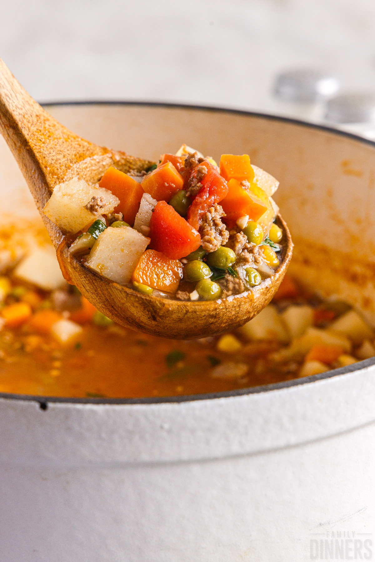 ladle scooping vegetable soup with ground beef out of a pot