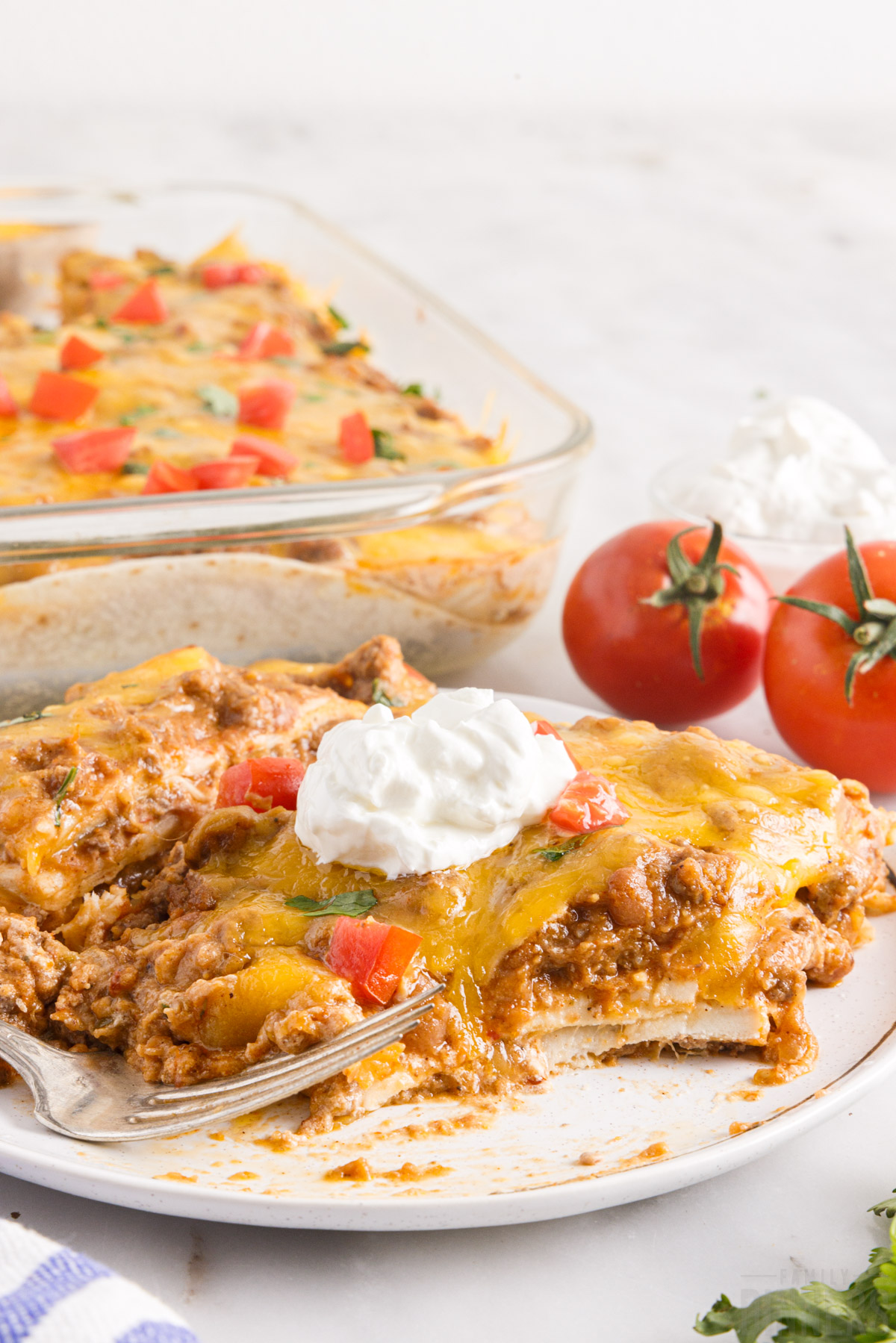 Mexican casserole on a plate with a dollop of sour cream and a fork