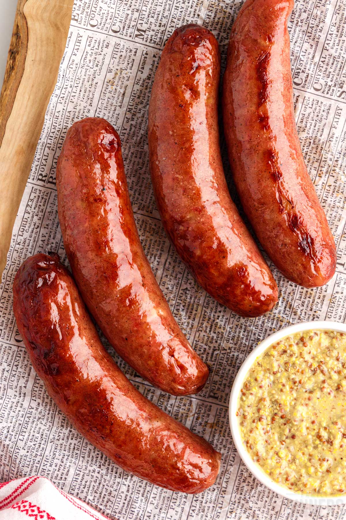 cooked sausage on a piece of paper with a bowl of mustard