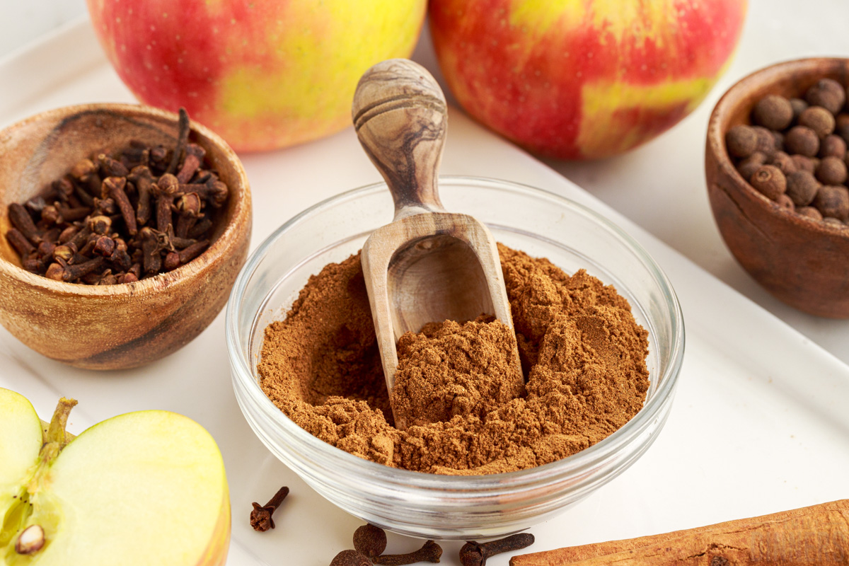 apple pie seasoning in a glass bowl with fresh apples, whole cloves and whole allspice