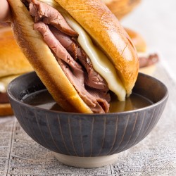 French dip being dipped into a small bowl of au jus.