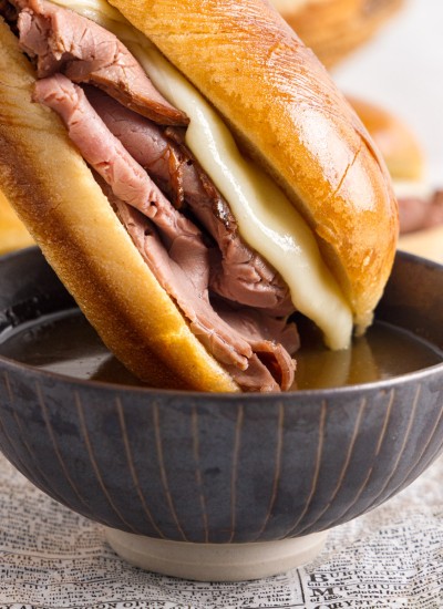 French dip being dipped into a small bowl of au jus.