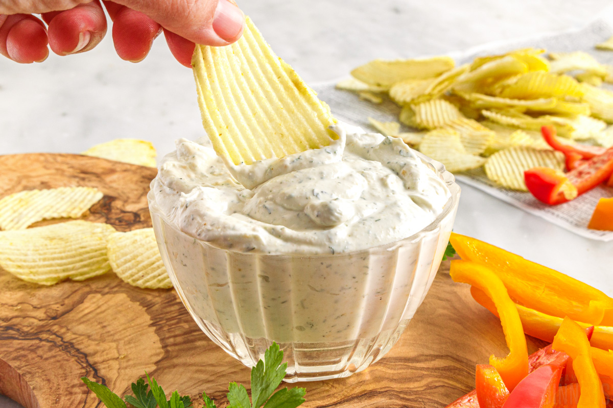 hand dipping a chip into ranch dip with chips and veggies on the side
