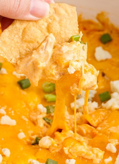 Chip dipping into cheesy buffalo chicken dip in a white crockpot.