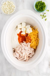 unmixed buffalo chicken dip ingredients in a slow cooker
