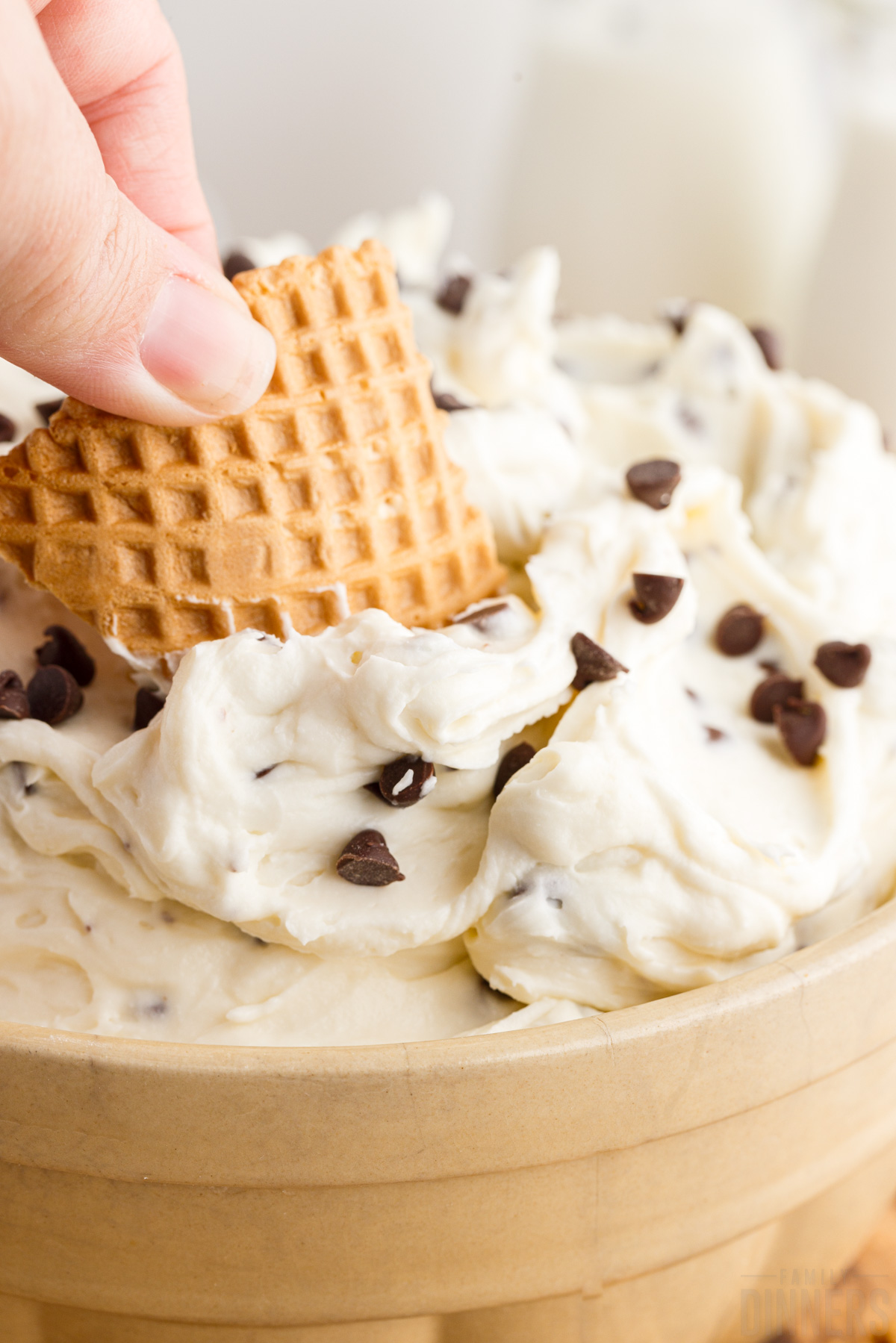 Waffle cookie being dipped into cannoli dip.