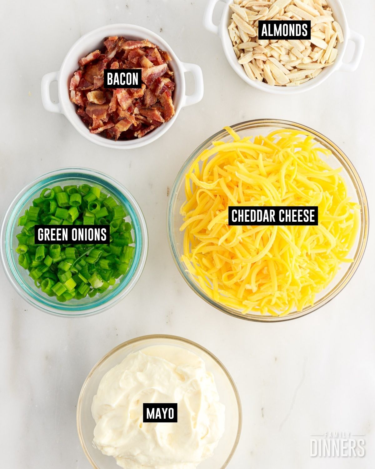 Labeled bowls of almonds, bacon crumbles, shredded cheddar cheese, green onion slices and mayonnaise. 