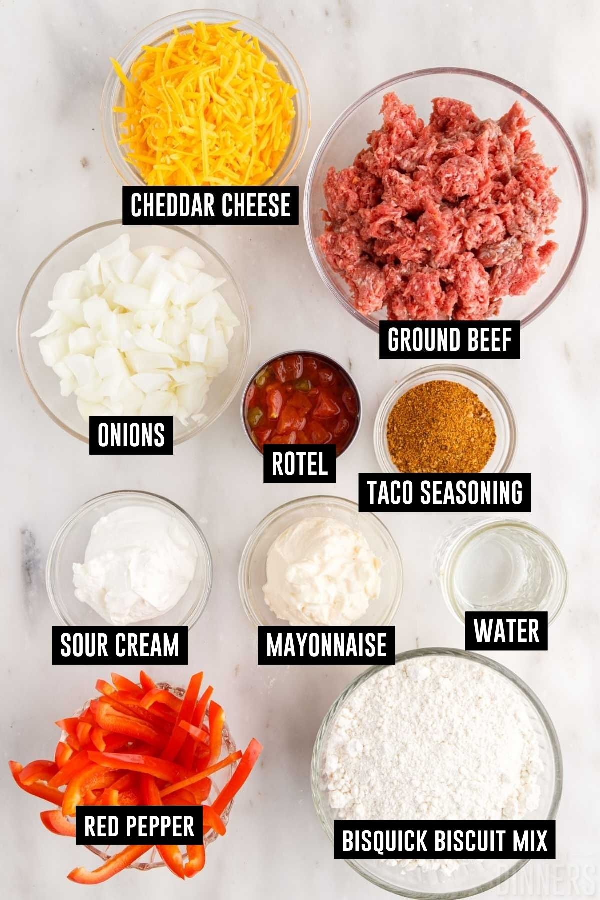 Ingredients for john wayne casserole in bowls including: ground beef, shredded cheese, chopped onions, rotel, taco seasoning, sour cream, mayonnaise, bell peppers and bisquick